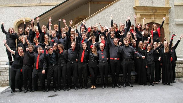 Eine Gruppe von jungen Frauen und Männern, schwarz bekleidet und mit roten Accessoires, vor der Treppe eines alten Gebäudes. Eine Gruppe von jungen Frauen und Männern, schwarz bekleidet und mit roten Accessoires, vor der Treppe eines alten Gebäudes.