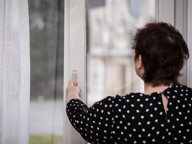 Eine Frau von hinten, die ein Bürofenster öffnet und in Kipplage bringt. Eine Frau von hinten, die ein Bürofenster öffnet und in Kipplage bringt.