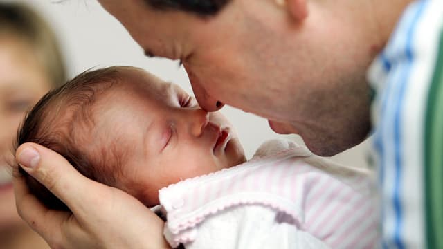 Ein Mann berührt mit seiner Nase die Nase eines schlafenden Babys, das er vor sich hält.