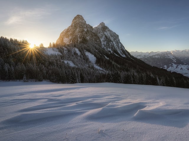 Die Sonne steigt neben den Gipfeln über den Horizoint, rundum liegt Schnee.