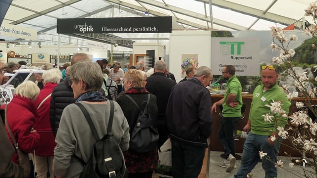 Zuschauer drängen sich zwischen Ständen eines Gartenbauers und Optikers Zuschauer drängen sich zwischen Ständen eines Gartenbauers und Optikers