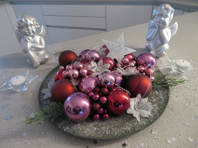 Zwei silberfarbene Engel schmücken ein Arrangement mit Weihnachtskugeln auf einem Teller.