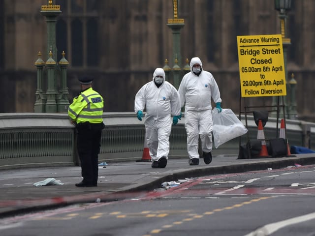 Zwei weiss gekleidete Forensiker gehen über die abgesperrte Brücke. Hinter ihnen das gelbe Warnplakat. Zwei weiss gekleidete Forensiker gehen über die abgesperrte Brücke. Hinter ihnen das gelbe Warnplakat.