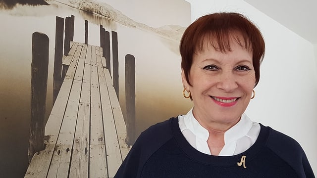 Eine Frau vor einem Bild, das einen Steg am See zeigt. Eine Frau vor einem Bild, das einen Steg am See zeigt.