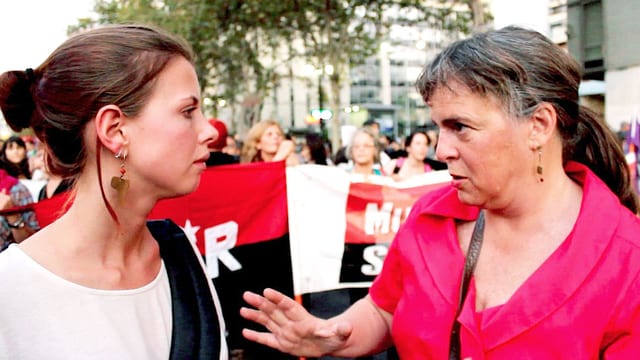 Eine Journalistin hört einer Frau zu, im Hintergrund ein Demonstrationszug. Eine Journalistin hört einer Frau zu, im Hintergrund ein Demonstrationszug.