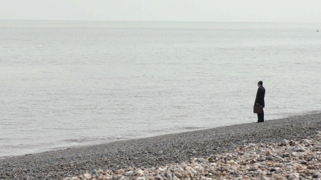 Ein Mann steht an einem Kieselstrand und blickt ins graue Meer hinaus. Ein Mann steht an einem Kieselstrand und blickt ins graue Meer hinaus.