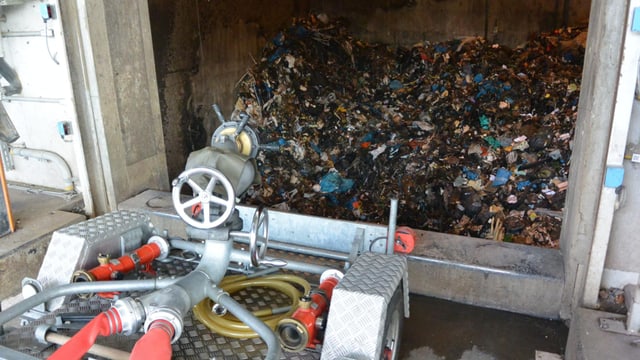 Feuerwehrschläuche, im Hintergrund verbrannter Kehricht in einem Lagerbunker Feuerwehrschläuche, im Hintergrund verbrannter Kehricht in einem Lagerbunker
