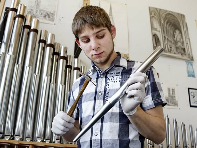 Der Instrumentenbauer klopft mit einem Hämmerchen auf eine kleine Orgelpfeife.