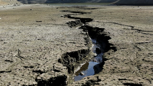 Bild von ausgetrockneter Erde. In der Mitte ein grosser Riss mit etwas Wasser drin. Bild von ausgetrockneter Erde. In der Mitte ein grosser Riss mit etwas Wasser drin.