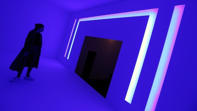 Eine Frau schaut sich eine pinke Lichtinstallation von James Turrell an. Eine Frau schaut sich eine pinke Lichtinstallation von James Turrell an.