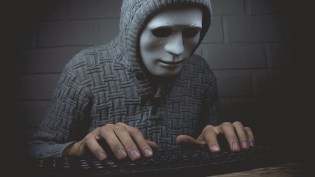Maskierte Person an einer Tastatur. Maskierte Person an einer Tastatur.