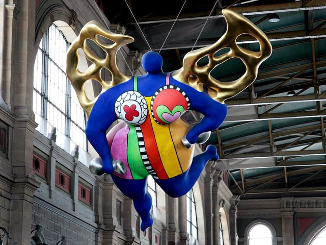 Eine farbenfrohe Figur, aufgehängt an der Decke der Bahnhofshalle in Zürich. Eine farbenfrohe Figur, aufgehängt an der Decke der Bahnhofshalle in Zürich.
