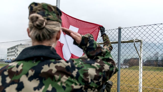 Eine Frau salutiert vor einer Schweizer Flagge Eine Frau salutiert vor einer Schweizer Flagge