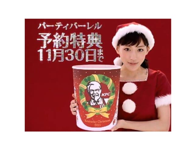 Eine Japanerin im Weihnachtsmann-Outfit hält einen Behälter der Fastfoodkette Kentucky Fried Chicken in die Kamera- Eine Japanerin im Weihnachtsmann-Outfit hält einen Behälter der Fastfoodkette Kentucky Fried Chicken in die Kamera-