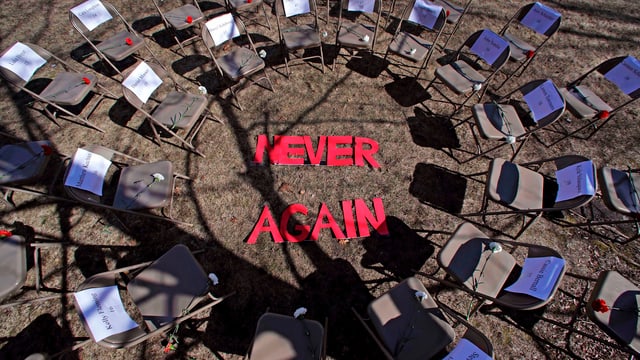 Ein Plenum mit leeren Stühlen und der Aufschrift "Never Again". Ein Plenum mit leeren Stühlen und der Aufschrift "Never Again".