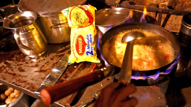 Maggi-Nudelpack auf einem Herd. Daneben eine Pfanne, in der die Nudeln kochen. Maggi-Nudelpack auf einem Herd. Daneben eine Pfanne, in der die Nudeln kochen.