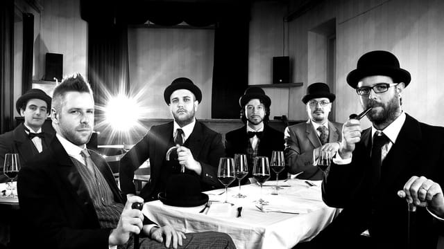 Die Band The Vad Vuc sitzt an einem Esstisch mit Melonen-Hüten