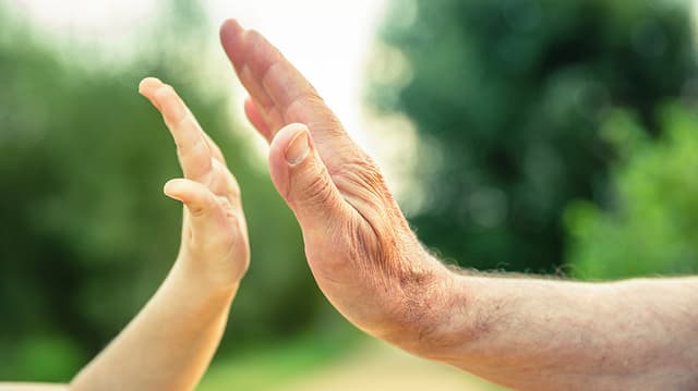 Eine Kinderhand und eine Hand einer älteren Person, die kurz davor sind, aufeinanderzuklatschen. Eine Kinderhand und eine Hand einer älteren Person, die kurz davor sind, aufeinanderzuklatschen.