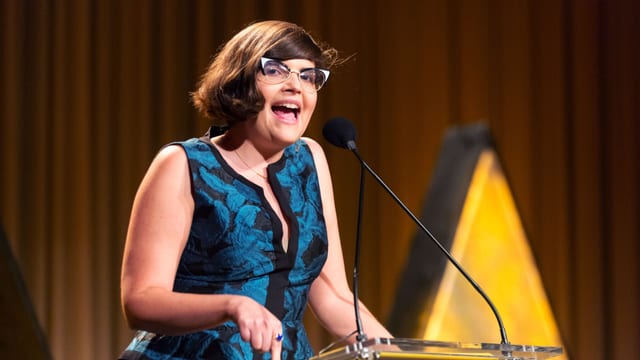 Eine junge Frau mit Brille an einem Rednerpult. Eine junge Frau mit Brille an einem Rednerpult.