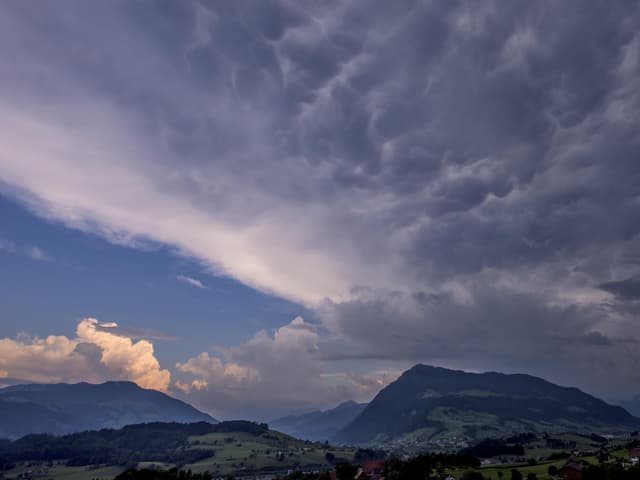 Landschaft mit Bergen. Am Himmel von rechts dunkle Wolken, links noch blau und sonnig.
