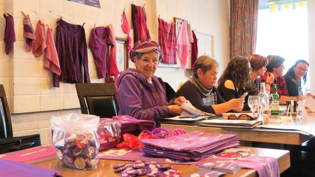 Eine Gruppe von Frauen, die an einem Tisch sitzen. Vor sich lilafarbene Anstecker und Prospekte Eine Gruppe von Frauen, die an einem Tisch sitzen. Vor sich lilafarbene Anstecker und Prospekte