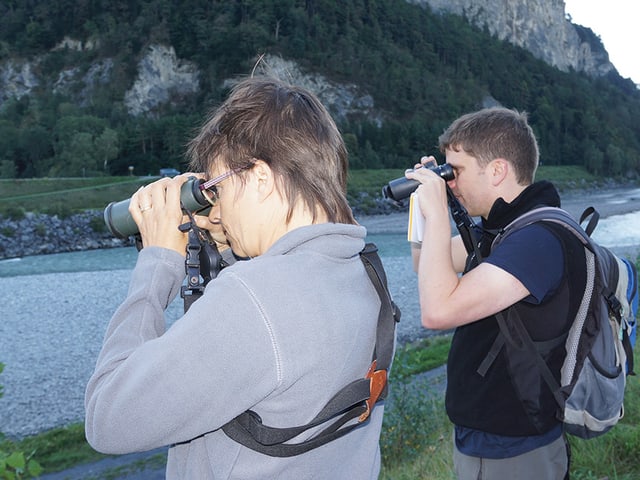 Eine Frau und ein Mann stehen mit einem Fernrohr am Flussufer. Eine Frau und ein Mann stehen mit einem Fernrohr am Flussufer.