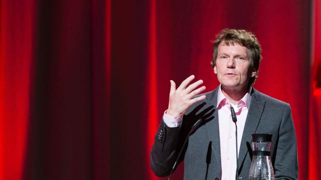 Hartmut Rosa in Anzug vor einem roten Vorhang bei einer Rede Hartmut Rosa in Anzug vor einem roten Vorhang bei einer Rede