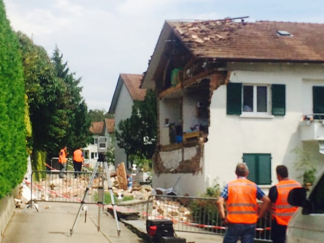 zerstörte Hausfassade, darum herum stehen Rettungskräfte mit oranger Weste
