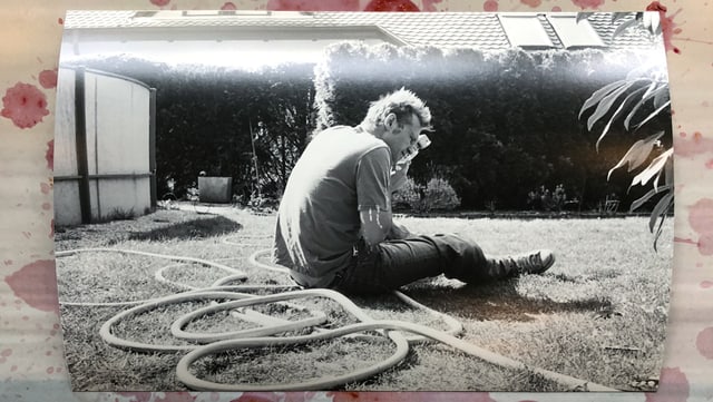 Mann sitzt halb abgewandt auf Rasen, Gartenschlauch neben ihm Mann sitzt halb abgewandt auf Rasen, Gartenschlauch neben ihm