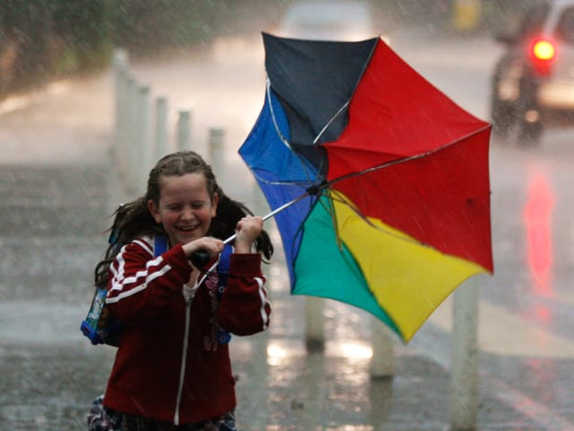 Mädchen auf der Strasse mit Regenschirm. Es regnet und windet. Der Schirm hat sich schon umgedreht und das Kind ist tropfnass.