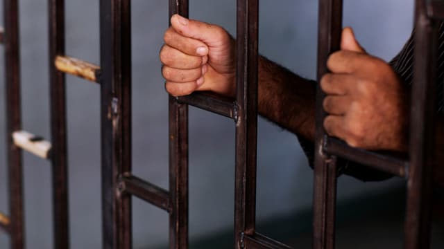Zwei Hände umklammern Gitterstäbe einer Zelle Zwei Hände umklammern Gitterstäbe einer Zelle