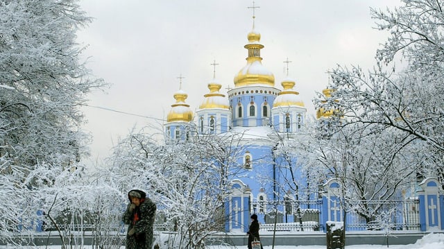 Ältere Frau stapft durch den Schnee vor einer Kathedrale mit goldenen Kuppeln. Ältere Frau stapft durch den Schnee vor einer Kathedrale mit goldenen Kuppeln.