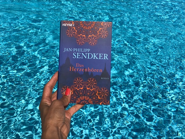 Annette König hält das Buch von Jan-Philip Sendker: «Das Herzhören» vor blaues Wasser Annette König hält das Buch von Jan-Philip Sendker: «Das Herzhören» vor blaues Wasser