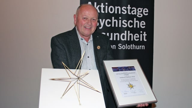 Ein Mann hält eine Urkunde und eine Auszeichnung in der Hand Ein Mann hält eine Urkunde und eine Auszeichnung in der Hand