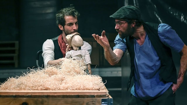 Zwei Männer auf einer Bühne: der eine hält eine Holzpuppe in den Händen. Zwei Männer auf einer Bühne: der eine hält eine Holzpuppe in den Händen.