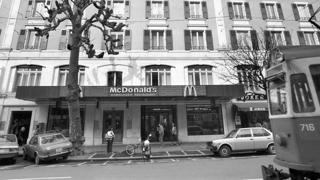 eine schwarz-weiss Aufnahme eines McDonalds in Genf, an der Strasse davor fährt ein Tram eine schwarz-weiss Aufnahme eines McDonalds in Genf, an der Strasse davor fährt ein Tram
