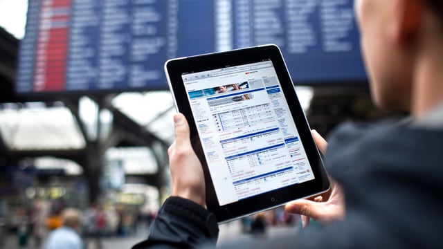 Ein Mann hält ein Tablet, im Hintergrund eine Zeittafel der SBB Ein Mann hält ein Tablet, im Hintergrund eine Zeittafel der SBB