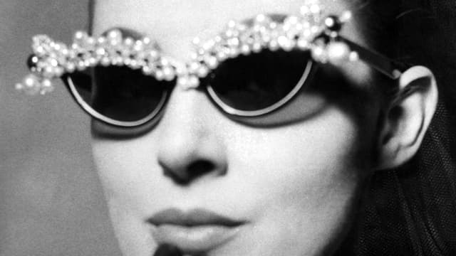 Eine Frau trägt eine schmetterlingsförmige Brille mit Perlen am oberen Rand. Eine Frau trägt eine schmetterlingsförmige Brille mit Perlen am oberen Rand.