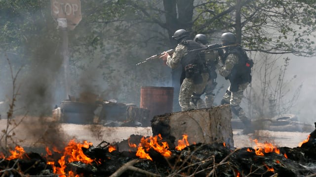 Bewaffnete Soldaten stehen vor brennenden Trümmern. Bewaffnete Soldaten stehen vor brennenden Trümmern.