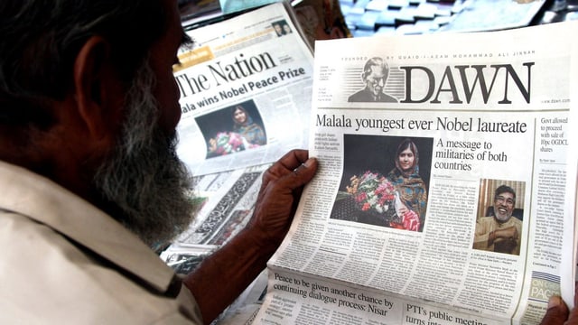 Ein Mann sieht sich die Titelseite einer Zeitung an, auf der ein Bild von Malala Yousafzai und ihrer Ehrung zu sehen ist. Ein Mann sieht sich die Titelseite einer Zeitung an, auf der ein Bild von Malala Yousafzai und ihrer Ehrung zu sehen ist.