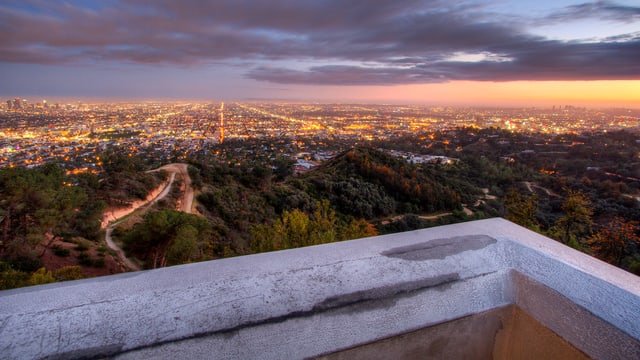 Blick von einem Balkon über die Millionenmetropole Los Angeles, deren Lichter in der Dämmerung schimmern.