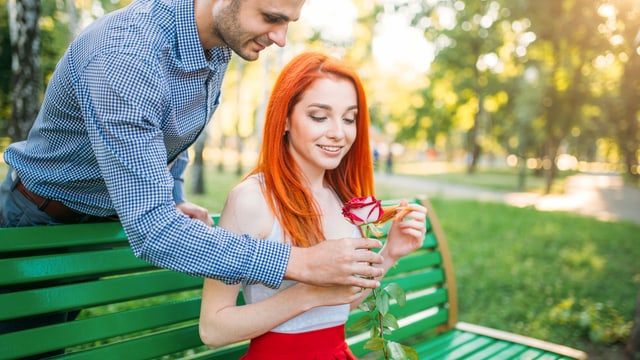 Mann steht hinter einer Frau und beschenkt sie mit einer Rose Mann steht hinter einer Frau und beschenkt sie mit einer Rose