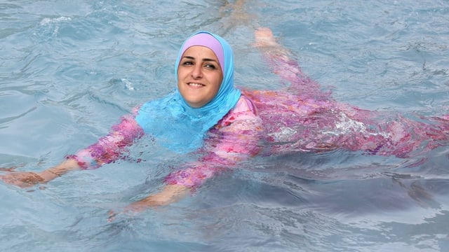 Eine junge, muslimische Frau schwimmt in einem Burkini.