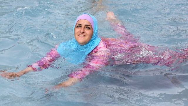 Eine junge, muslimische Frau schwimmt in einem Burkini. Eine junge, muslimische Frau schwimmt in einem Burkini.