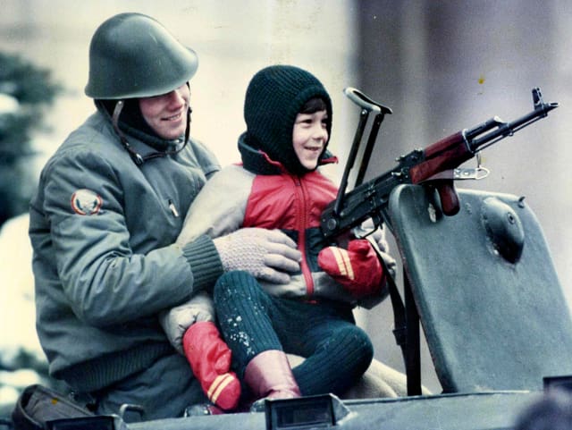 Soldat mit Kind auf Panzer sitzend, ein lächelndes Kind auf dem Schoss haltend