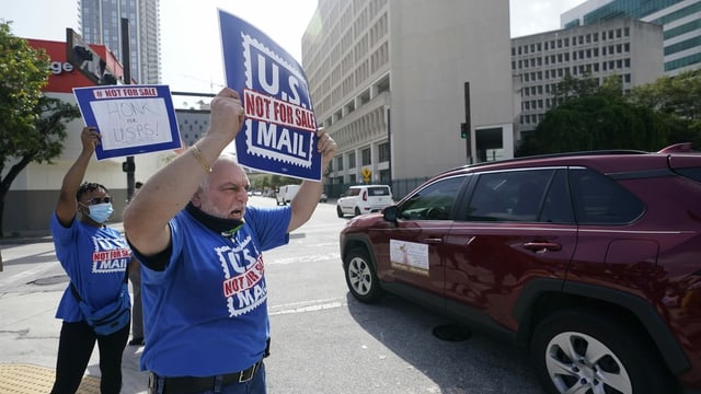 Zwei Personen demonstrieren mit Schildern gegen Änderungen bei der US-Post. Zwei Personen demonstrieren mit Schildern gegen Änderungen bei der US-Post.