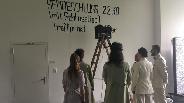 Schauspieler vor einer Wand auf der "Sendeschluss" geschrieben steht. Schauspieler vor einer Wand auf der "Sendeschluss" geschrieben steht.