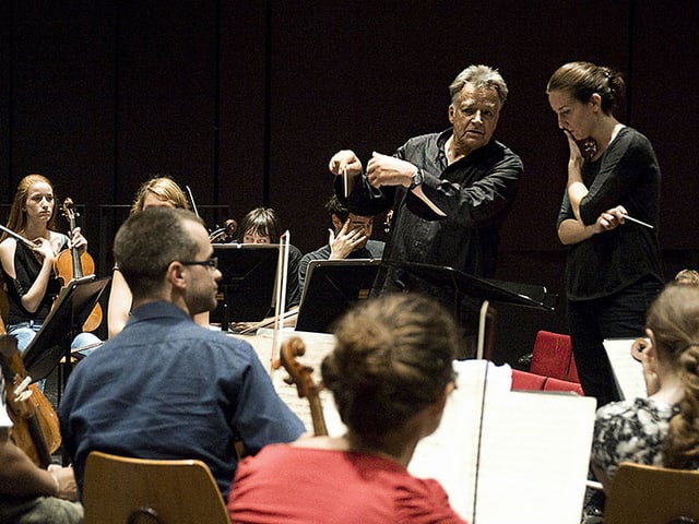 Der Dirigent umbegen von Musikerinnen und Musikern an einer Probe. Der Dirigent umbegen von Musikerinnen und Musikern an einer Probe.