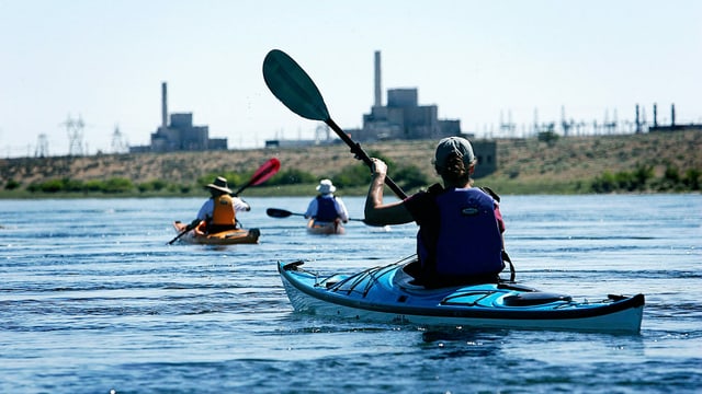 Drei Leute paddeln in Kayaks auf einem Fluss. Drei Leute paddeln in Kayaks auf einem Fluss.