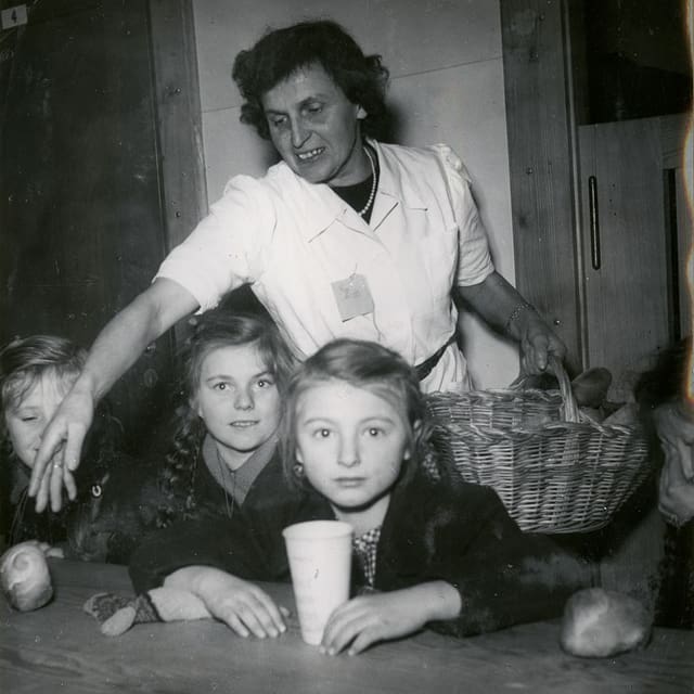 Eine Frau steht hinter Kindern, die an einem Tisch sitzen. Eine Frau steht hinter Kindern, die an einem Tisch sitzen.